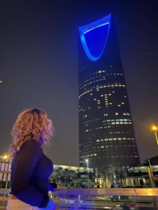 Woman standing at night in Riyadh looking at Kingdom Centre Tower with city lights and skyline view