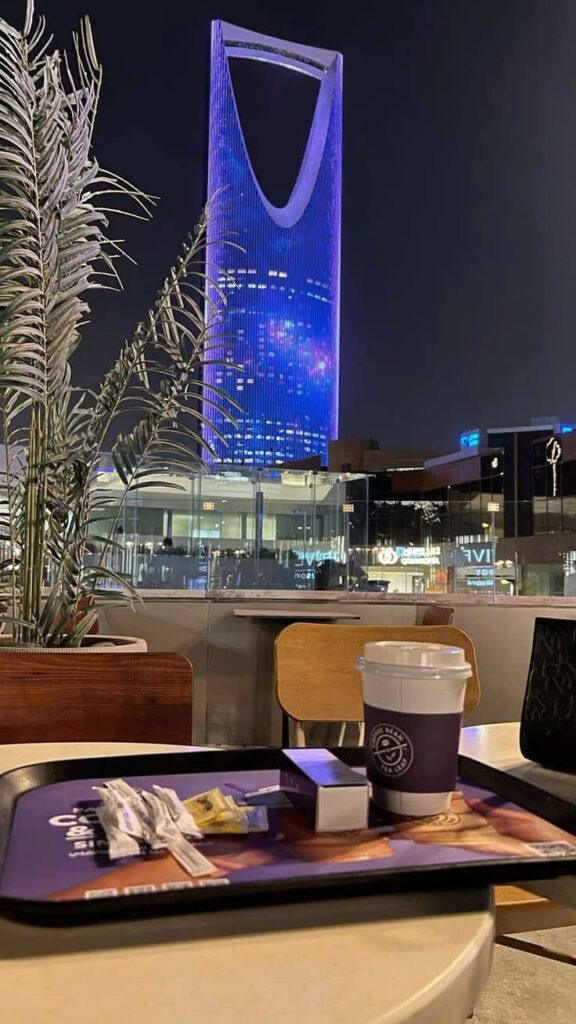 Girls sitting at a cafe watching Kingdom Centre Tower at night in Riyadh with city lights and skyline view